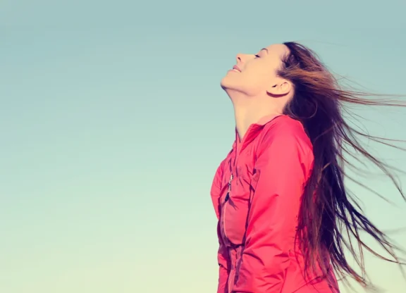 woman-smiling-looking-up-to-blue-sky-taking-deep-breath-celebrating-freedom