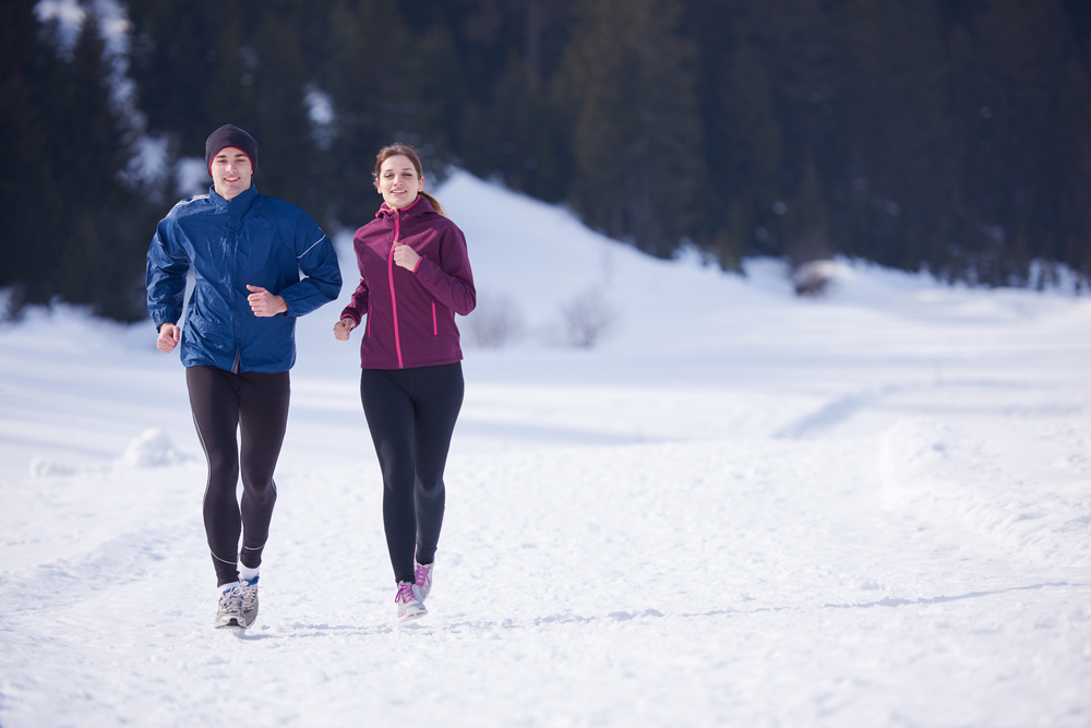 healthy young couple jogging outside on snow in forest. athlete running on beautiful sunny winter day